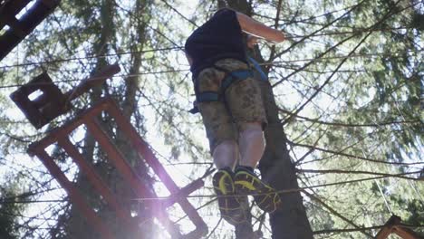 young man in safety equipment walking on rope on high in summer climbing park