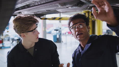 male tutor with student looking underneath car on hydraulic ramp on auto mechanic course