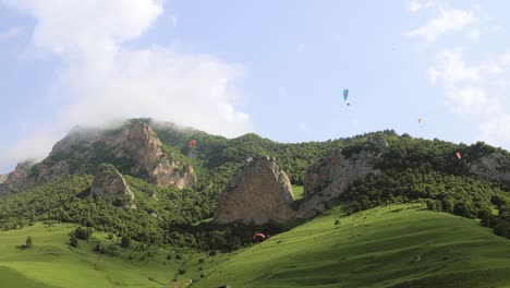 los pilotos de parapente vuelan parapentes entre nubes y montañas verdes.