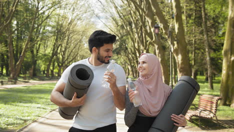 couple exercising in park with yoga mats and water bottles