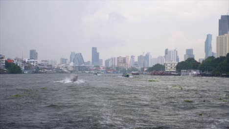 slow motion shot of the chao phraya river in bangkok taken from a boat. other boats are visible on the water and the skyscrapers of the city are visible in the background