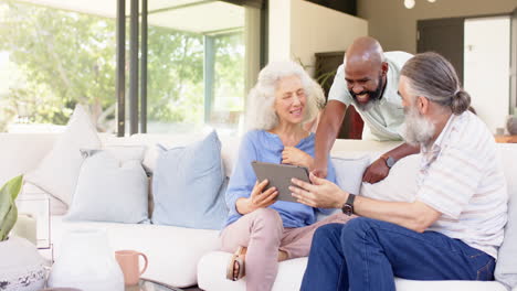 senior friends using tablet and laughing together on sofa in living room