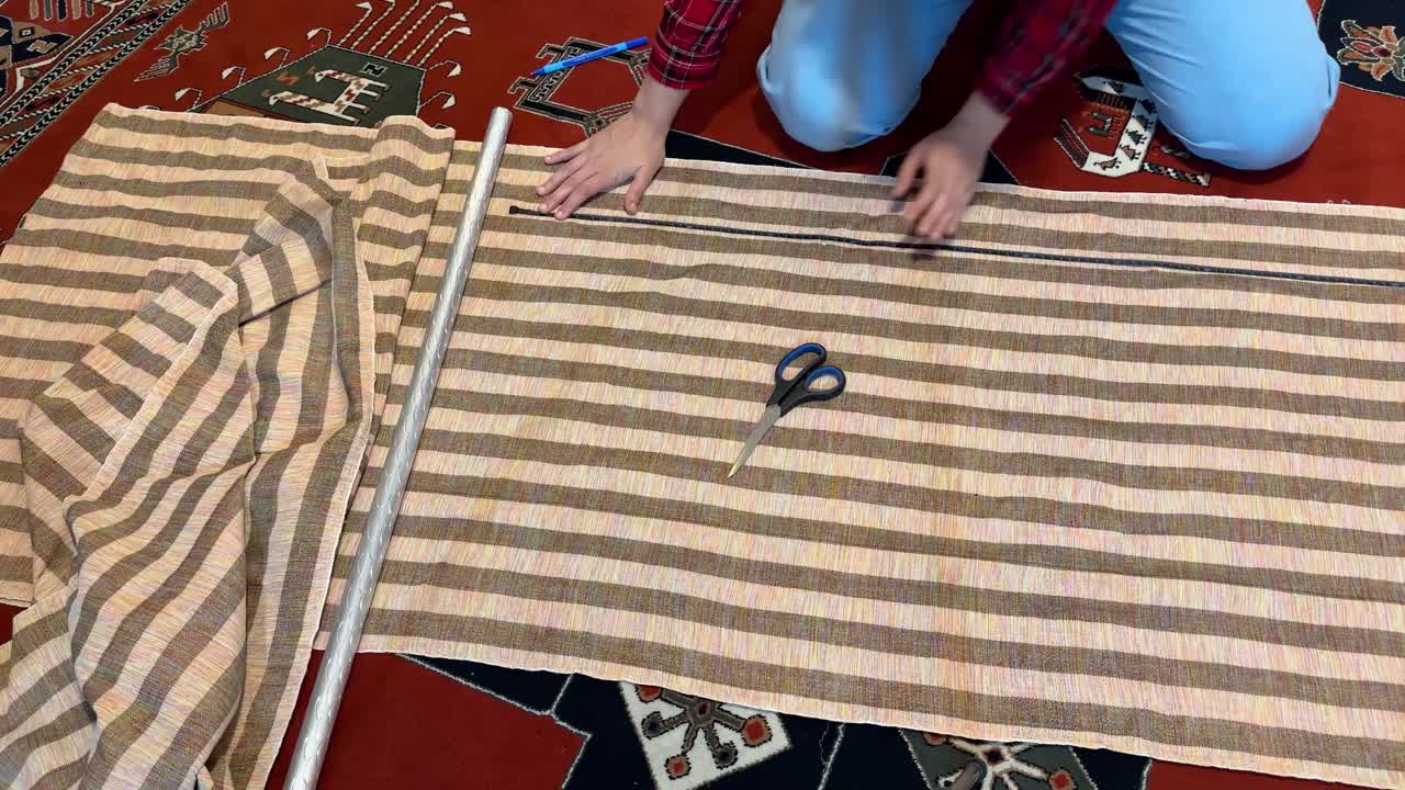 A woman sit on a Red Persian carpet do tailoring meter and measure the fabric to cut curtain cloth and sewing attach two parts to cover decoration of the house in rural area in middle east asia