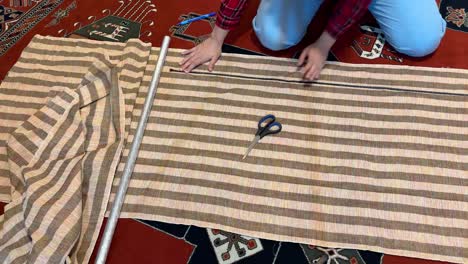 a woman sit on a red persian carpet do tailoring meter and measure the fabric to cut curtain cloth and sewing attach two parts to cover decoration of the house in rural area in middle east asia