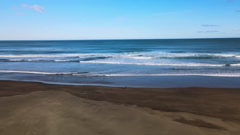 Cinematic-pan-of-surfers-walking-along-shoreline-on-Piha-black-sand-beach-in-New-Zealand's-West-coast