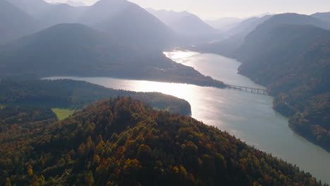 autumnal woodland mountain peak aerial view towards emerald sylvenstein lake reflecting sunrise