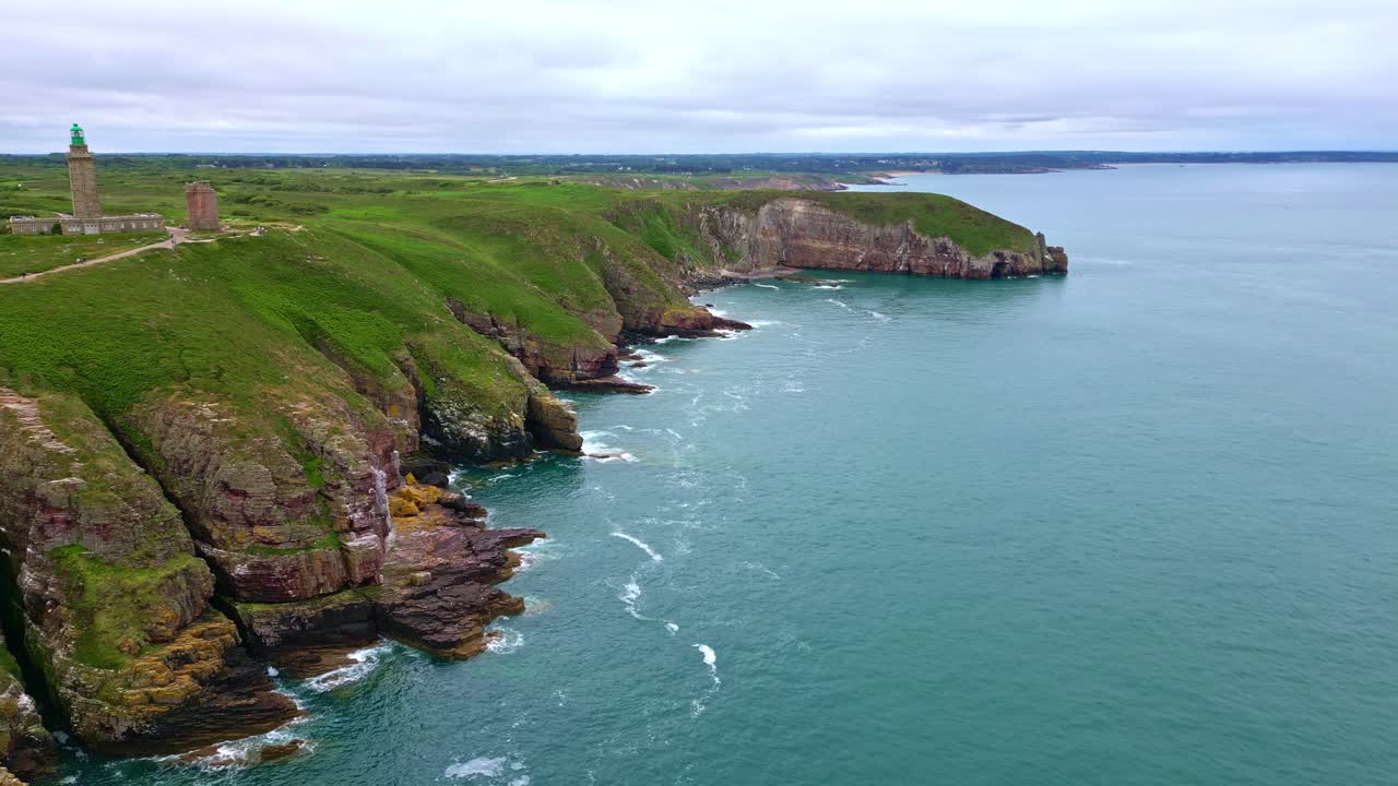 Cliffs and green headland of Cap Fréhel, with lighthouse in distance, Brittany, France, Scenic nature, coastline. Aerial forward, copy space