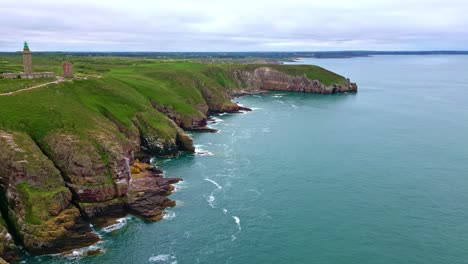 cliffs and green headland of cap fréhel, with lighthouse in distance, brittany, france, scenic nature, coastline. aerial forward, copy space