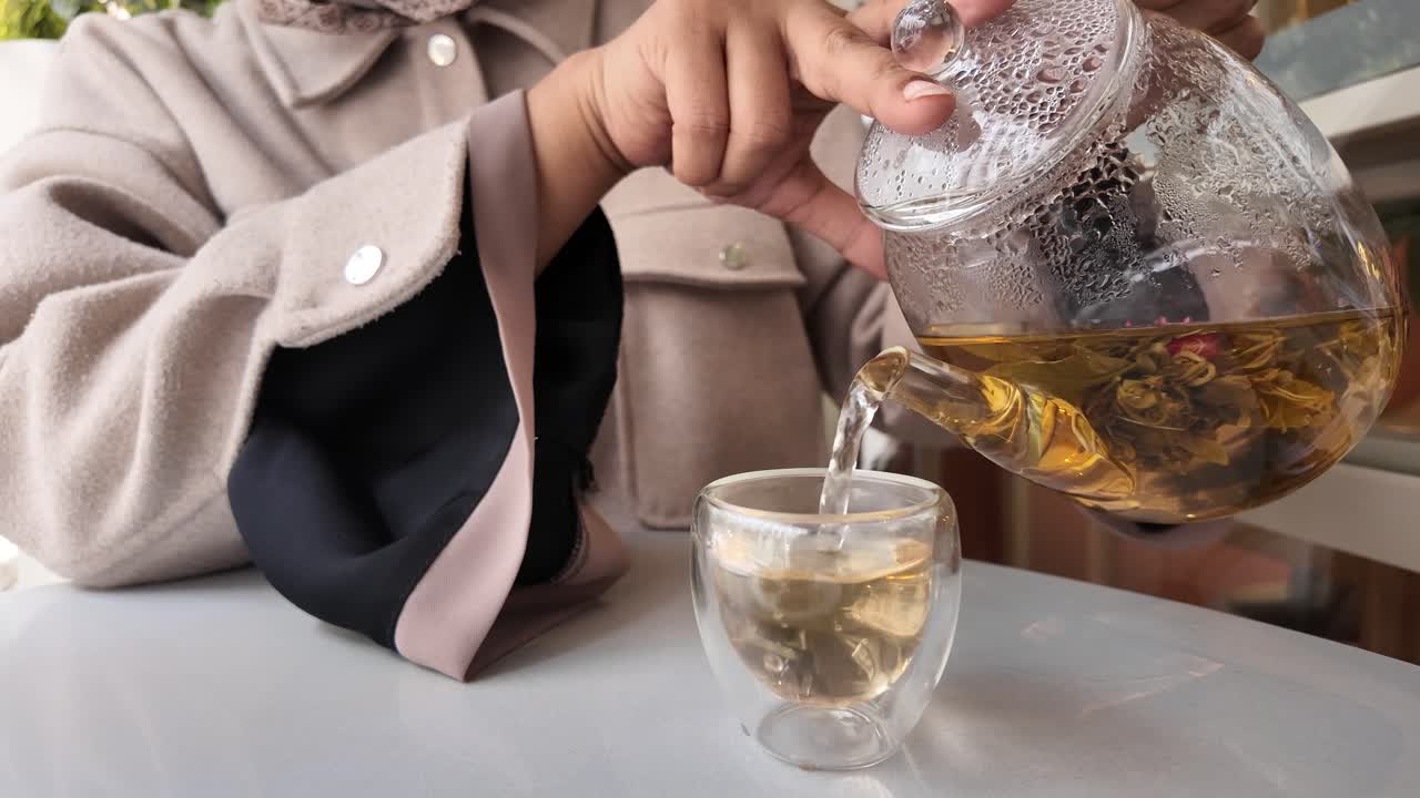 Pouring tea from a glass teapot into a glass cup