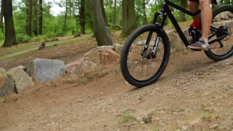 un jinete en una bicicleta de trekking de montaña negra pasando por un giro brusco en un sustrato de arcilla en medio del bosque y recubriendo piedras más pequeñas al lado de un giro en cámara lenta 120fps