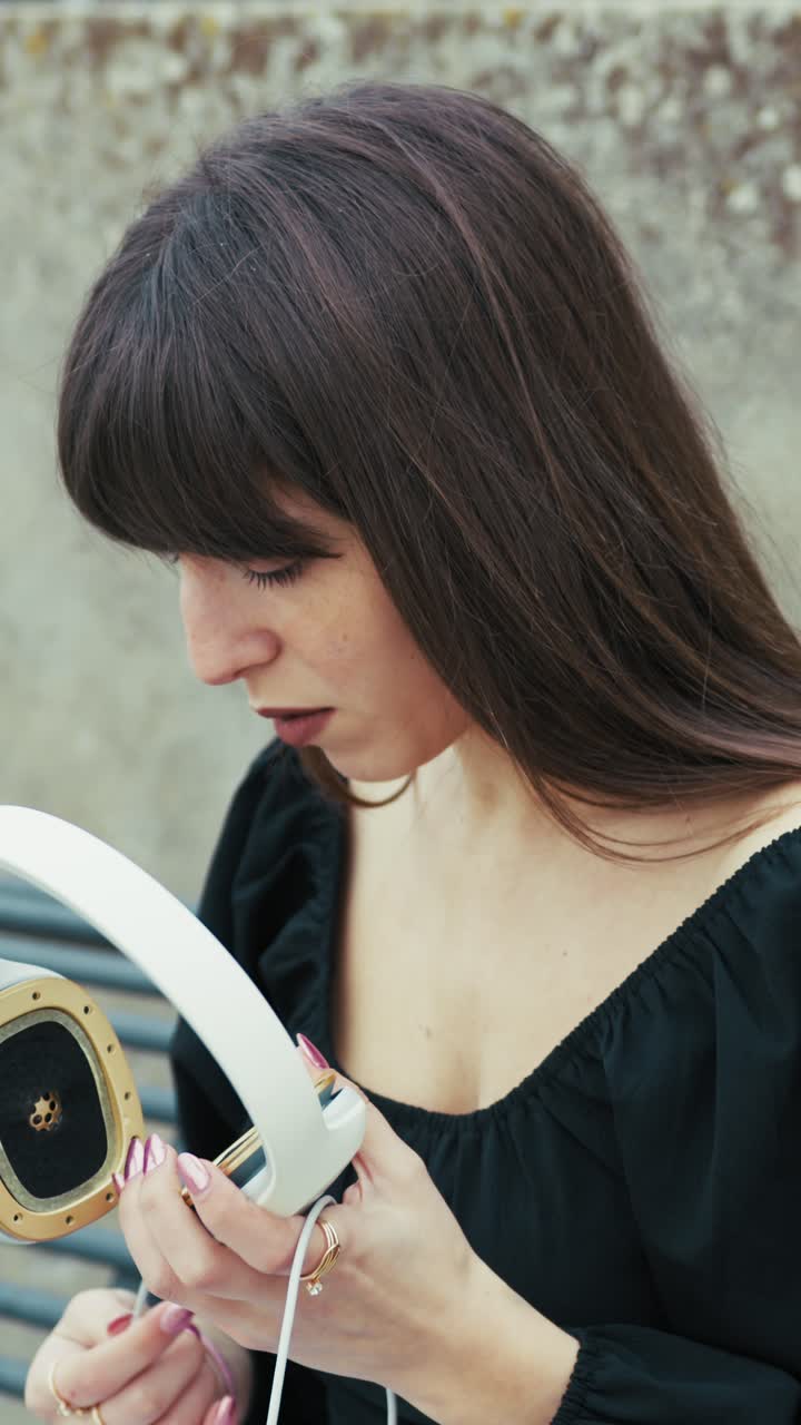 Woman Picking up Off The Headphones While Sitting On The Bench Outdoor