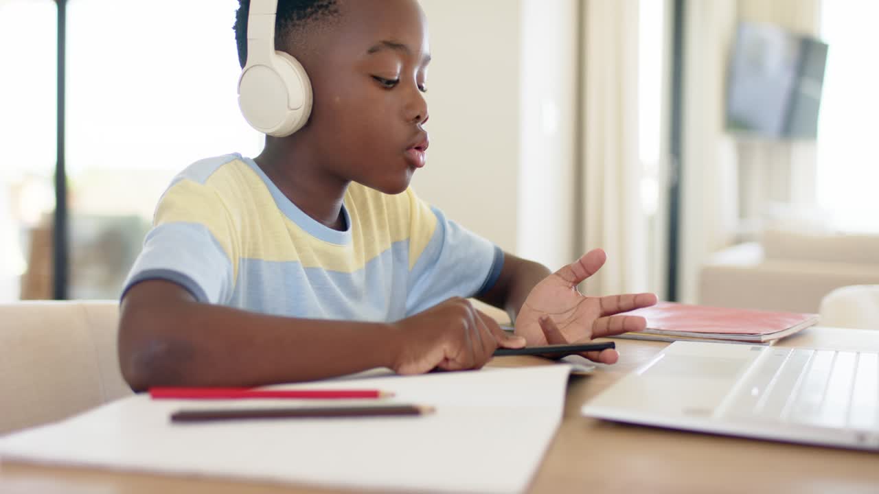 African American boy in headphones tapping pencil on palm at home desk while following audio lesson