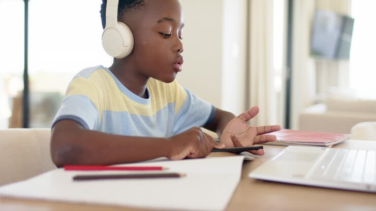 African American boy in headphones tapping pencil on palm at home desk while following audio lesson