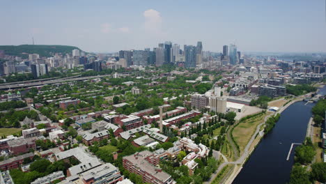 Aerial-view-flying-along-the-Lachine-Canal,-tilting-toward-the-skyline-of-Montreal