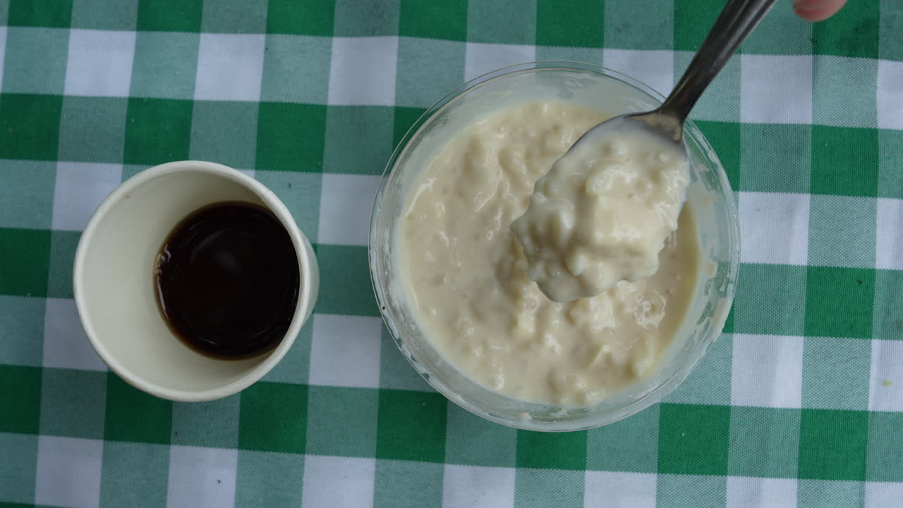 Veduta dettagliata di cremoso Arroz de Leche mescolato accanto a una tazza di ricco caffè colombiano su una tovaglia a quadri, che mette in risalto i sapori tradizionali