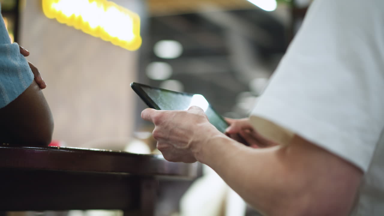 Blurry shot of restaurant storefront sign glowing in yellow and white colours with indistinct brand logo while silhouettes of people passing by across foreground handheld camera creates dynamic vibes