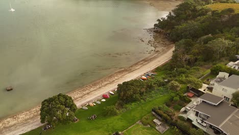 aerial approaching shot of shelly beach with villas buildings in surfdale town, haiheke island. sunset time in the evening. top down.