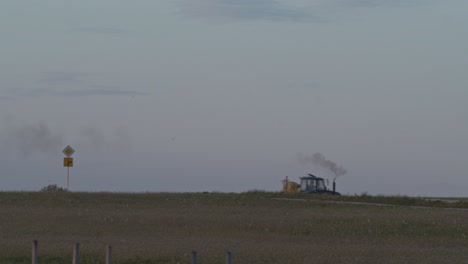 A-tractor-quickly-moving-across-the-frame-in-a-field-in-Poland,-wide-shot