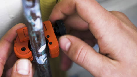 male hands fit a pipe cutter around an old broken copper pipe