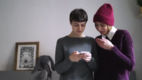 Two-woman-in-stylish-sweater-looking-photo-on-smartphone.-Female-friends-gossip