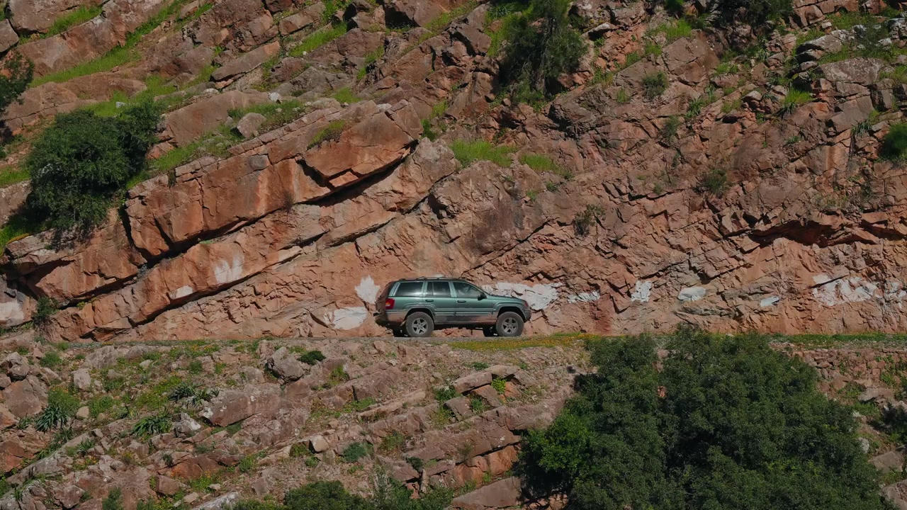 Green SUV driving a narrow rocky mountain track across a steep cliff face in the Atlas Mountains