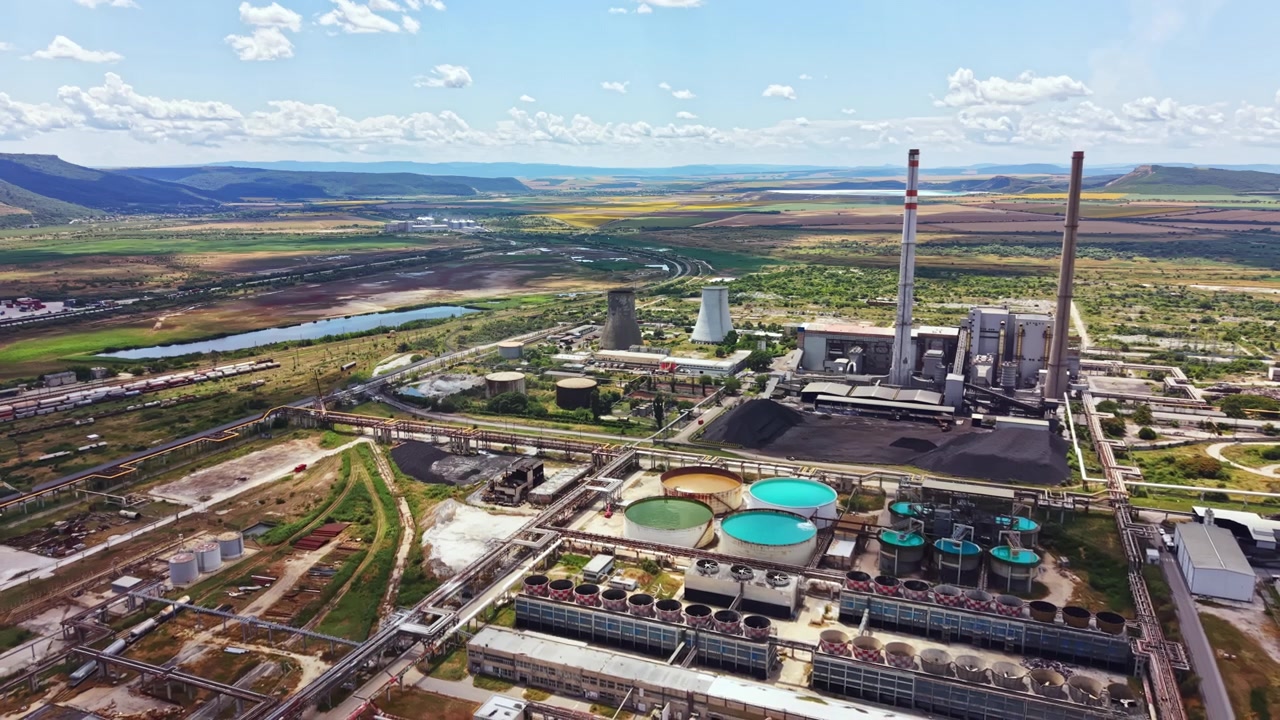 Power plant operations in an industrial area near a river with mountains in the background on a sunny day