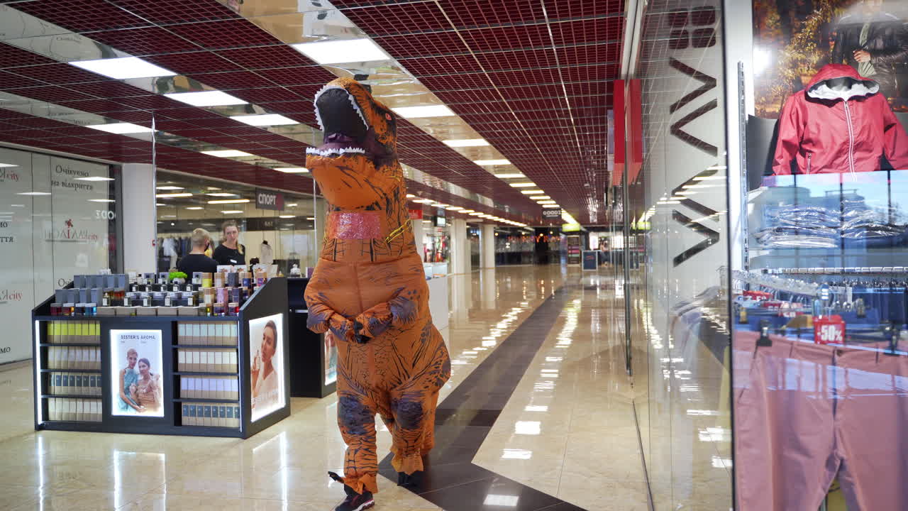 Animator in dinosaur inflatable costume walking quickly by the mall. Orange spotted T-Rex doing shopping in department store.