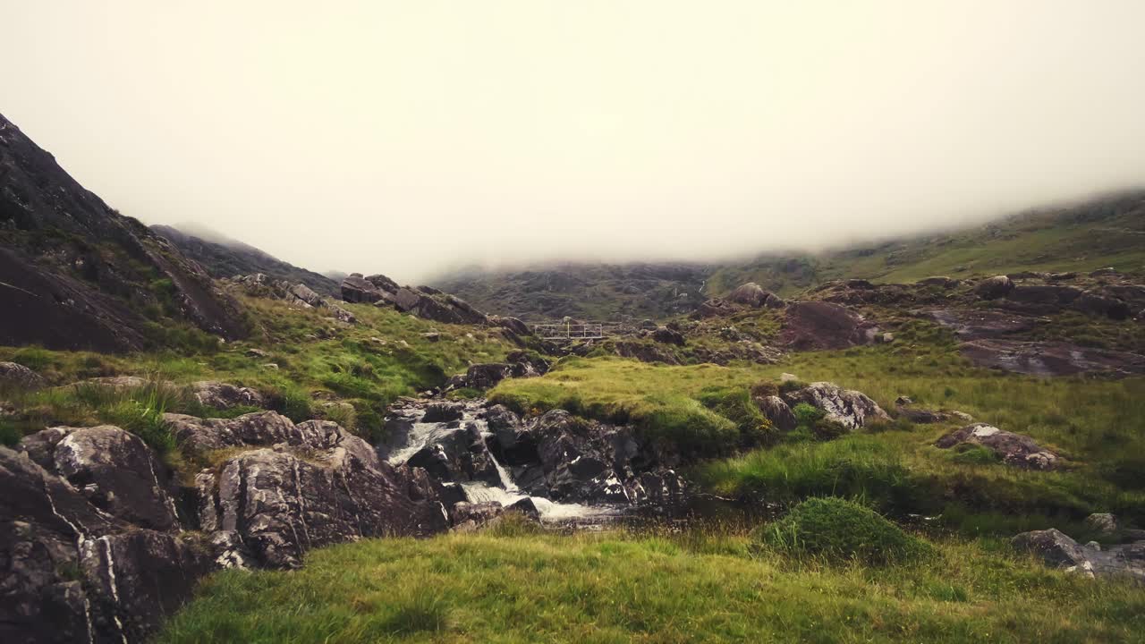 Landscape view of rugged lush green mountains with a creek flowing down, Ireland, on a rainy and foggy day