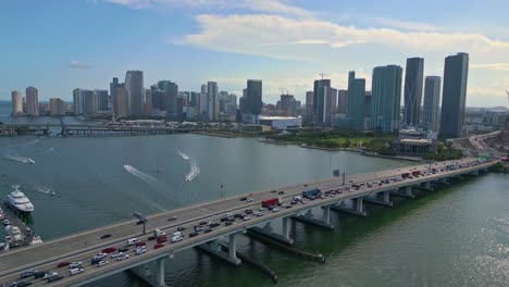 Tráfico-Elevado-En-El-Puente-Icw-De-Macarthur-Causeway-Con-Vista-Hacia-El-Horizonte-Del-Centro-De-Miami,-Clima-Soleado