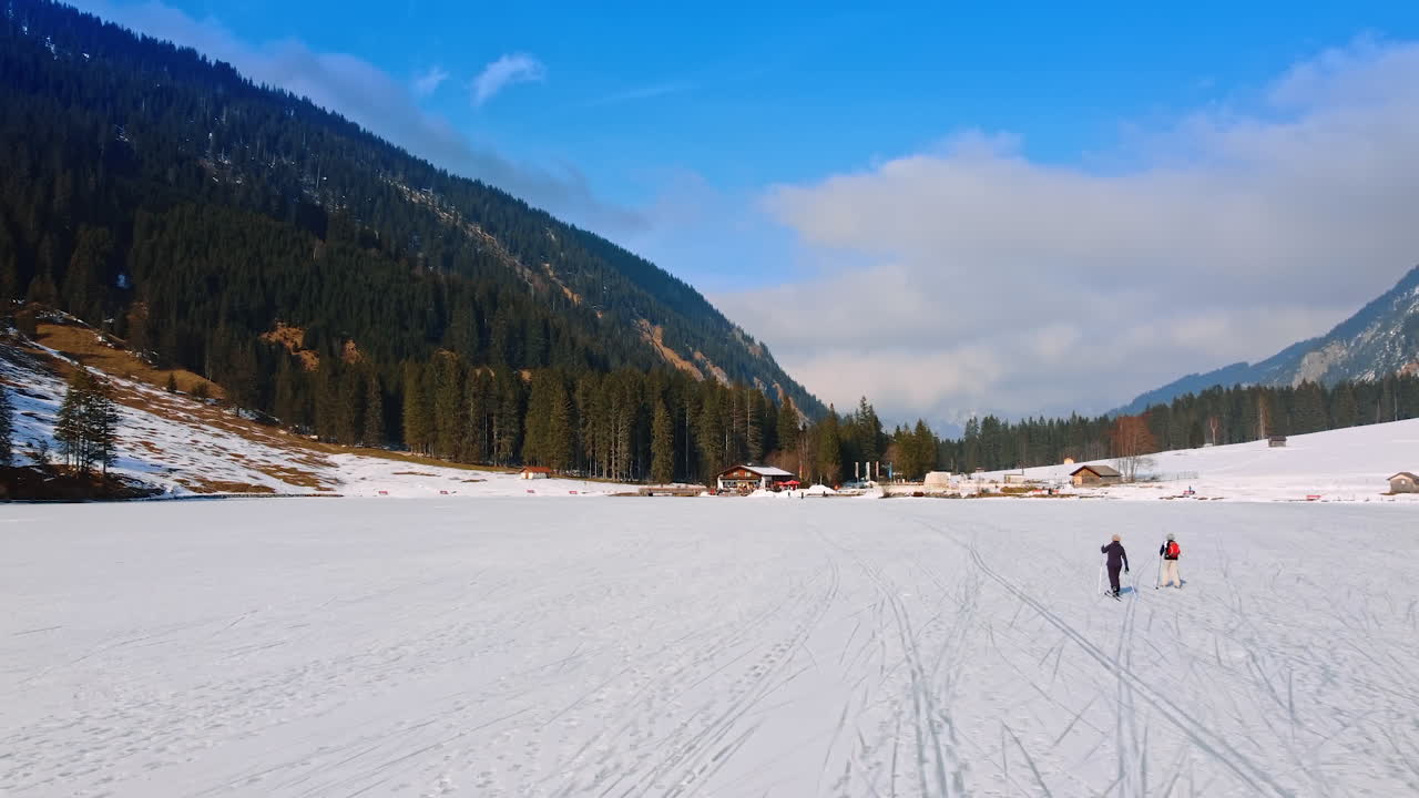 Couple skiing at the foot of the mountain covered with pine-tree forest. Skiing resort in the Swiss Alps. Lichtenstein nature.
