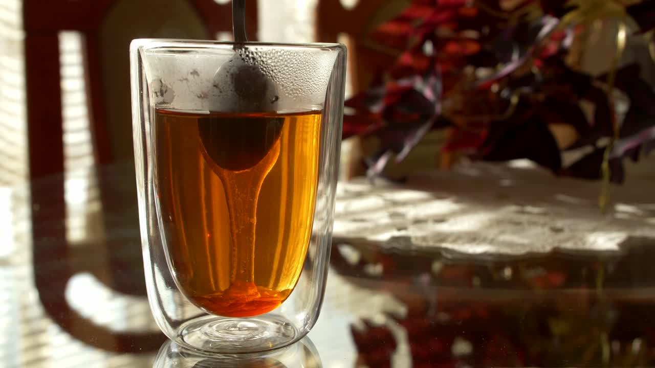 Close-up of a cup of tea with honey or sugar being added