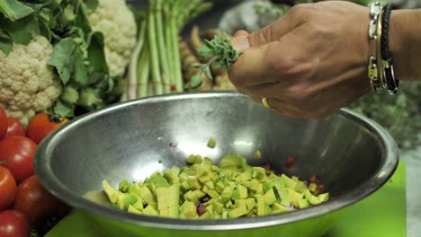 Adding-fresh-marjoram-leaves-to-chopped-vegetables,-preparing-vegetarian-meal