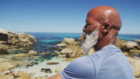 retrato de un anciano afroamericano sonriente haciendo ejercicio sentado en rocas junto al mar