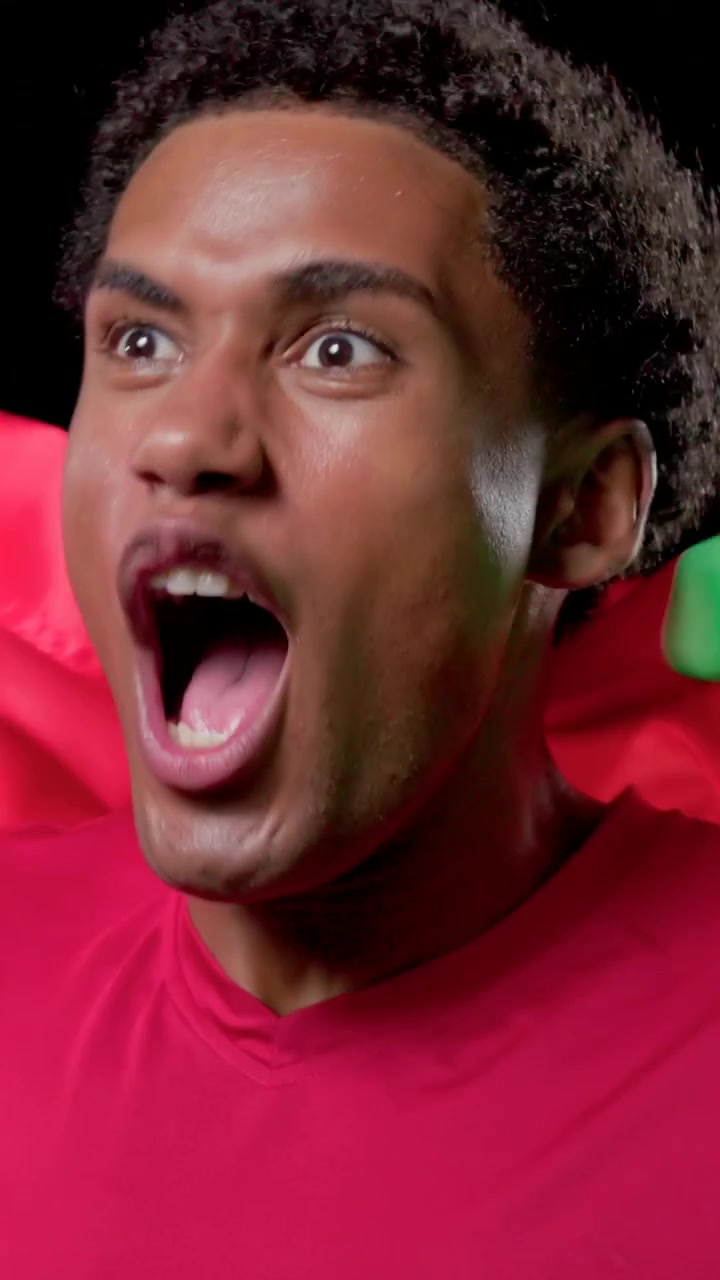 Vertical video: Waving man in red tee shouting after green red fabric crosses frame in black studio