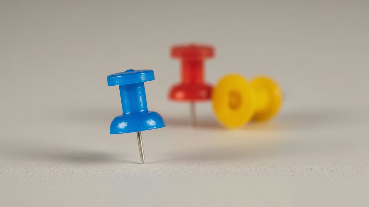 Wobbling blue plastic push pin oscillating on beige tabletop, with stationary red and yellow pins