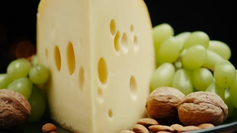 close up part of medium hard cheese head edam gouda parmesan on wooden board, with nuts and grapes rotaiting on the plate