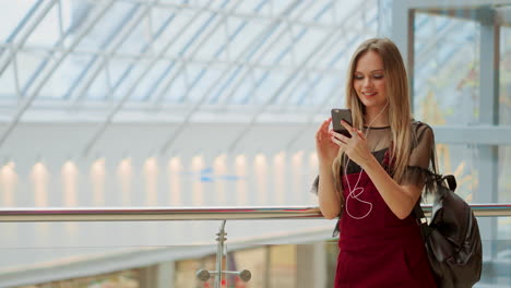 Una-Adolescente-Feliz-Sosteniendo-Bolsas-Con-Compras,-Sonriendo-Mientras-Mira-El-Teléfono-En-El-Centro-Comercial.-Recibí-Buenas-Noticias,-Leí-Un-Mensaje-Y-Envié-Mensajes-De-Texto.-Banner-Fotográfico-Horizontal-Para-El-Diseño-Del-Encabezado-Del-Sitio-Web