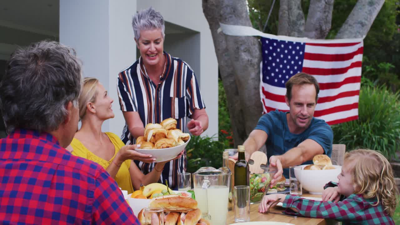 웃는 백인 고위 여성은 정원에서 함께 축하 식사를 하는 가족을 섬긴다.