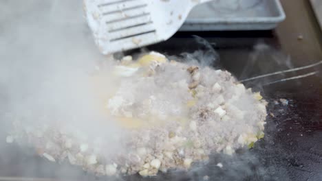 mixing in eggs as they cook and set with ground sausage, hash potatoes and cooked vegetables on the flat top griddle