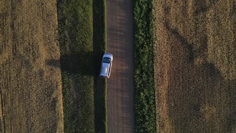 Aerial-zenith-view-of-silver-car-parked-on-dirt-road-then-heading-off-while-camera-is-following-from-above