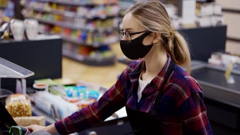 Female-cashier-in-a-protective-mask-pierces-the-products-with-the-scanner