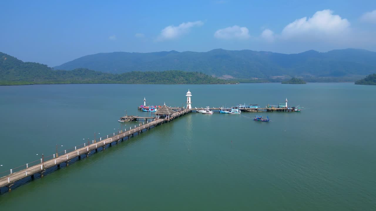 white lighthouse, long way pier extending into the bay with numerous boats docked and tropical islands in the background. Amazing aerial view panorama orbit drone