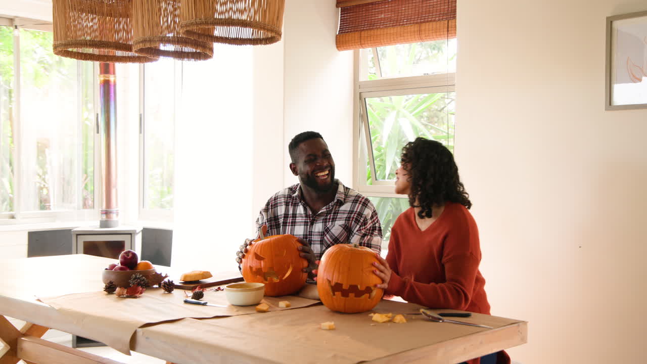Halloween time, multiracial couple carving pumpkins at home, enjoying festive autumn activity