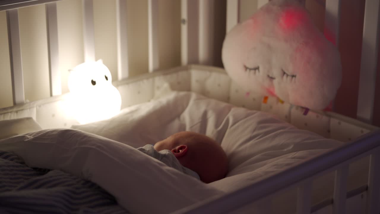 새로 태어난 아기가 저녁에 침대에서 잠을 자고, 3 주 된 아기는 밤 램프의 빛에 있습니다.