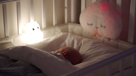 newborn baby boy sleeping in bed in the evening, 3-week-old infant in light of a night lamp.