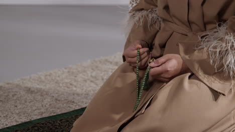 close up of muslim woman with prayer beads at home praying kneeling on prayer mat