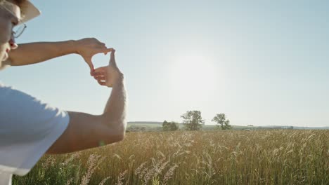 young man in a hardhat visualising a new project as he stands overlooking an agricultural field of golden cereal making a frame gesture with his hands