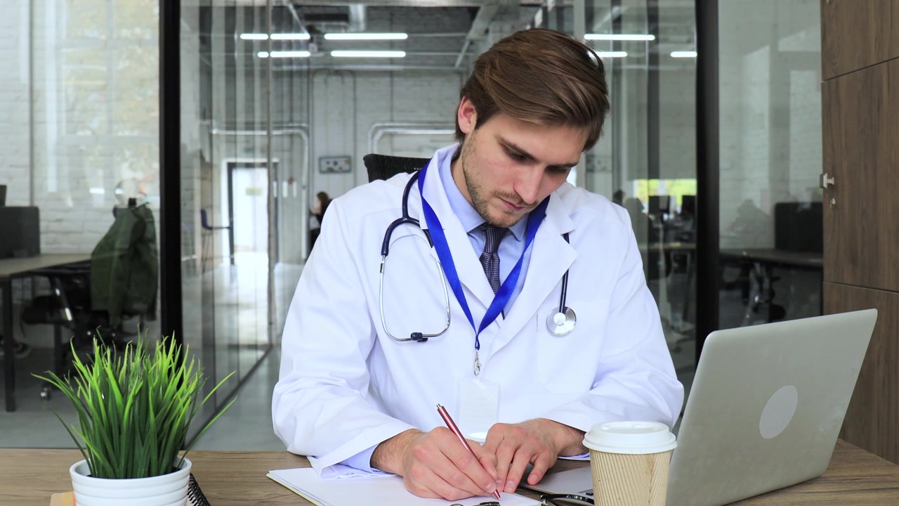 Giovane medico in camice bianco che lavora alla scrivania con il laptop