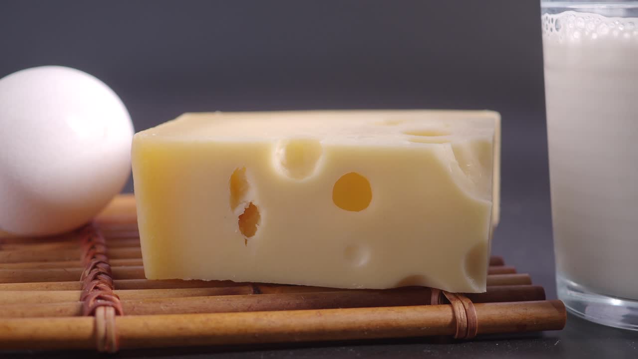 primer plano de un bloque de queso suizo, un huevo blanco y un vaso de leche