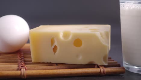 close-up of a block of swiss cheese, a white egg, and a glass of milk